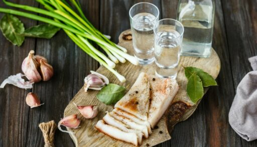 Соленое сало лежит на столе рядом с чесноком и напитками