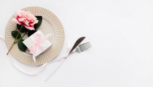 На столе лежит тарелка, цветы, вилка с ножом