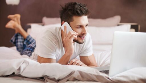 Молодой мужчина звонит по телефону, лежа на кровати