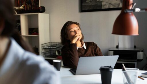 Молодая женщина задумчиво смотрит в окно офиса