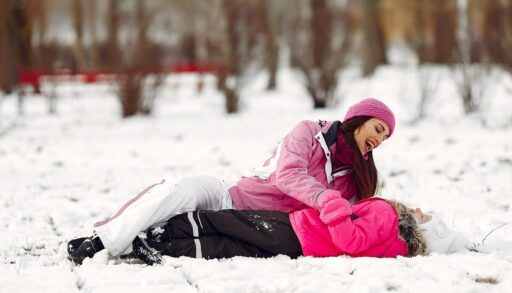 Мама с веселой девочкой играют на снегу