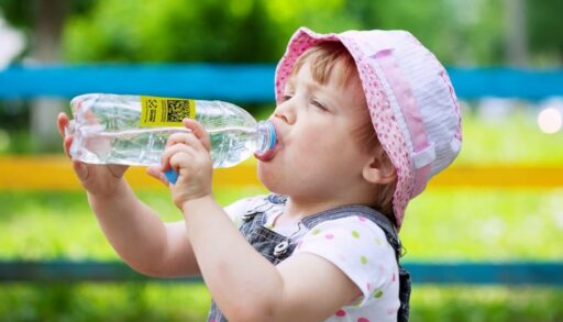 Маленькая девочка пьет воду из бутылки
