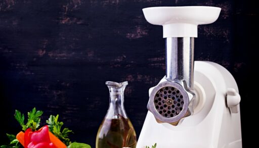 Электрическая мясорубка стои на столе рядом с маслом и овощами