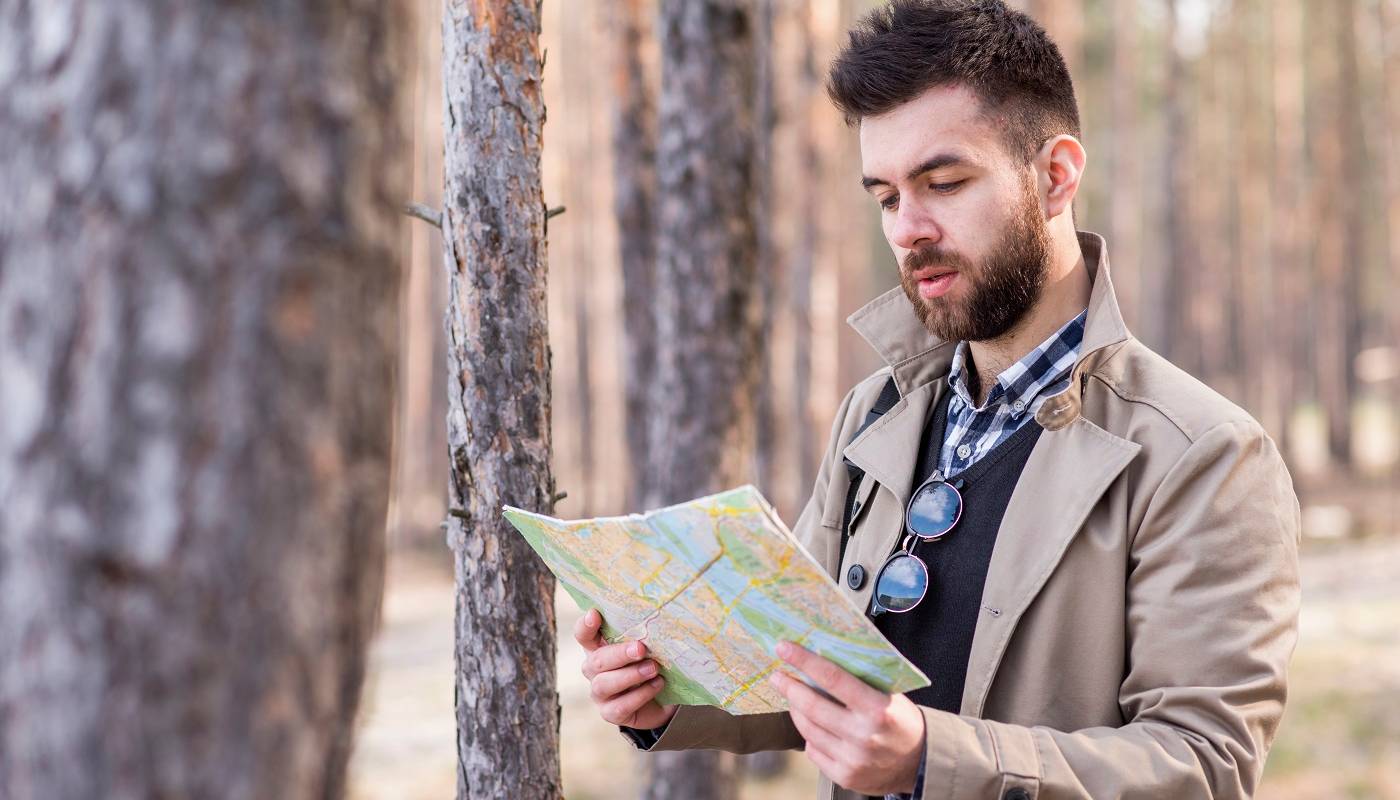 Молодой мужчина-путешественник определяет местоположение на карте