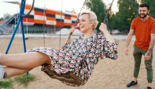 Молодой человек качает на качелях привлекательную девушку