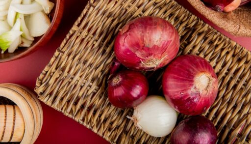 Красные луковицы лежат на плетеной доске